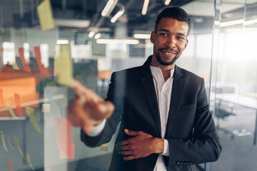 Businessman showing on sticky notes on glass wall while working in modern office