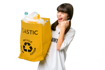 Little caucasian girl holding a bag full of plastic bottles to recycle over isolated background celebrating a victory