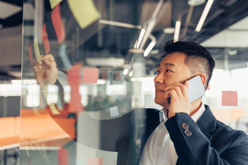 Businessman writing on sticky notes on glass wall while working in modern office