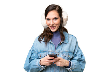 Young caucasian woman wearing winter muffs over isolated background sending a message with the mobile