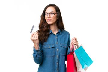 Young caucasian woman over isolated background holding shopping bags and a credit card and thinking