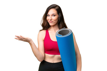 Young sport woman going to yoga classes while holding a mat over isolated background having doubts...