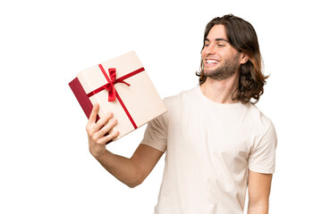 Young handsome man holding a gift over isolated background with happy expression