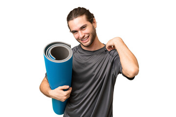 Young sport man going to yoga classes while holding a mat over isolated background laughing © luismolinero