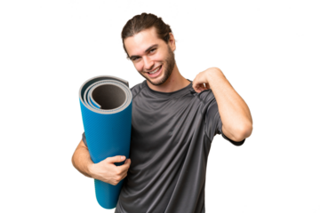 Young sport man going to yoga classes while holding a mat over isolated background laughing