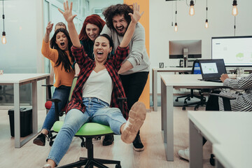 Team building and office fun. Young cheerful businesspeople in smart casual wear having fun while racing on office chairs and smiling.