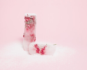 Frozen red flower on bright pastel pink background decorated with snow. Cold winter season concept with copy space. Creative ice blossom frost. Minimal nature Christmas winter snowy freeze.
