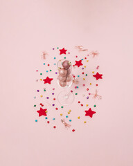 Champagne glass with baubles decorated with colorful confetti and red star on bright pastel pink background. Christmas or New Year party concept. Minimal winter holiday season idea.