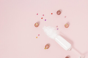 Champagne glass with snow decorated with baubles on bright pastel pink background. Christmas or New Year party concept. Minimal winter holiday season idea with copy space.