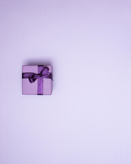 Purple gift box with ribbon on pastel purple background with copy space. Creative realistic minimal gift for Christmas or Holiday giving. Present with bow as Christmas gift.