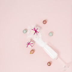 Minimal composition with champagne glass, snow, pink and green baubles, wrapped present against pastel pink background. Creative Christmas decoration with gift box. New Year party aesthetic style.