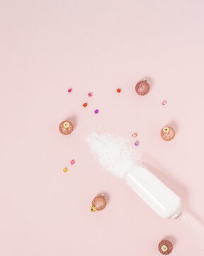 Champagne glass decorated with snow and  baubles on bright pastel pink background. Creative Christmas or New Year party concept. Minimal winter holiday season idea.