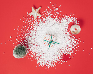 New Year winter arrangement made of Christmas ornament, tree, gift box decorated with snow. Christmas flat lay aesthetic concept on bold red background.