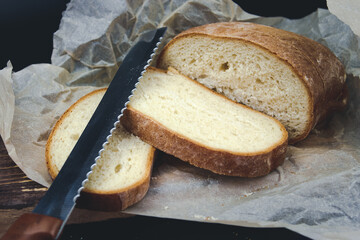 Fresh bread and knife on a black background. A loaf of fresh sliced brown bread on a bread board and a sharp knife