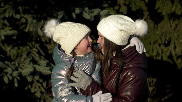 Young woman and a girl of 7-8 years old tenderly hug each other. Mom m daughter on a walk in the winter forest. Family holiday.