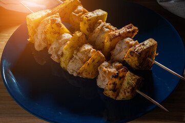 Grilled chicken pineapple kebab on skewers with spices in a blue plate on a wooden