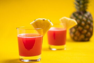 Pineapple juice in glass closeup near sliced fruit with spash and dripping liqid for summer vibes.