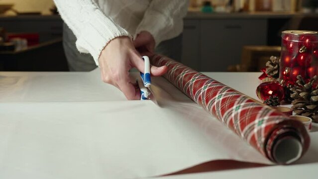 Close up of hands cutting off craft paper with scissors for wrapping gift for winter holidays. Preparation presents for relative and friend