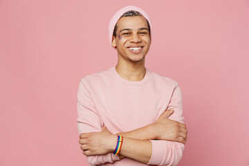 Young happy smiling cheerful fun gay man wear sweatshirt hat hold hands crossed folded look camera isolated on plain pastel light pink color background studio portrait. Lifestyle lgbtq pride concept.