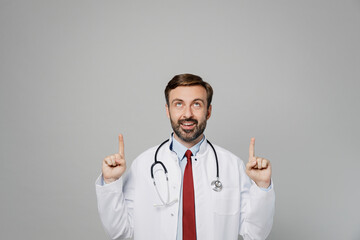 Male doctor happy man wears white medical gown suit stethoscope work in hospital point index finger above on worspace area isolated on plain grey color background studio. Healthcare medicine concept.