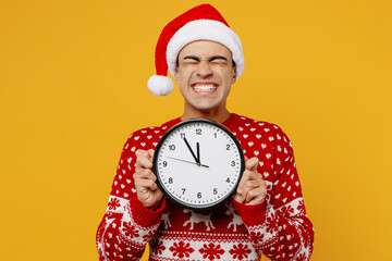Merry young man wear red knitted christmas sweater Santa hat posing hold clock show time five to...