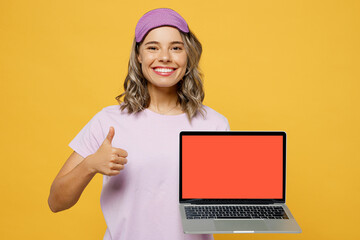 Young IT woman wears purple pyjamas jam sleep eye mask rest relax at home work use blank screen laptop pc computer show thumb up like isolated on plain yellow background Comfortable night nap concept.