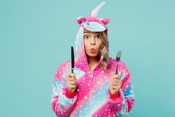 Young shocked woman 20s wear domestic costume with hoody and animals ears hold spoon and fork going to eat late evening isolated on plain pastel light blue cyan background. People lifestyle concept.