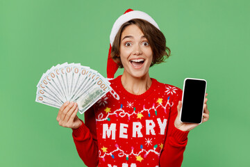 Merry young woman wear xmas sweater Santa hat posing hold blank screen mobile cell phone fan cash...