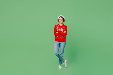 Fototapeta na wymiar Full body merry young woman wear xmas sweater Santa hat posing hold hands crossed folded look camera isolated on plain pastel light green background. Happy New Year 2023 celebration holiday concept.