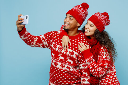 Merry young fun couple two man woman wear red Christmas sweater Santa hat posing do selfie shot on mobile cell phone isolated on plain pastel light blue background Happy New Year 2023 holiday concept