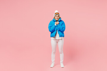 Snowboarder sad frozen woman wearing blue suit goggles mask hat hold ski padded jacket warming herself isolated on plain pastel pink background. Winter extreme sport hobby weekend trip relax concept.