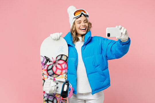 Snowboarder fun woman wear blue suit goggles mask hat ski padded jacket doing selfie shot on mobile cell phone isolated on plain pink background. Winter extreme sport hobby weekend trip relax concept.