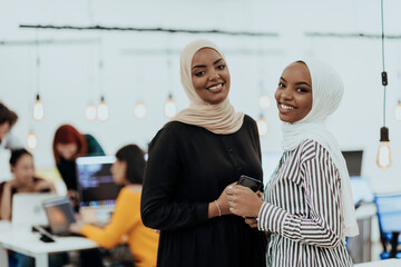 Portrait of two African American businesswomen talking to each other while standing in a modern business office with their colleagues. Marketing concept. Multi-ethnic society.