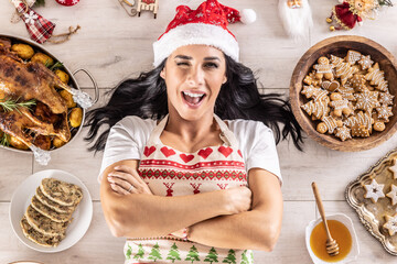 Blinking dark-haired female cook in a Christmas apron and Santa hat lying on the floor, surrounded...