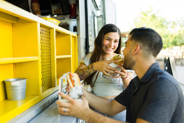 Beautiful hungry couple laughing while eating at the food truck