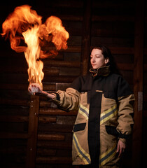A woman holds a fire in her hand. Flame, portrait, looks at the fire, wooden background, fire suit, flame in the form of a bird, magic