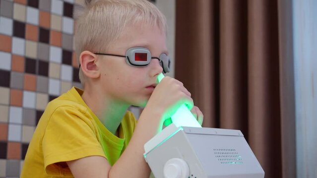 A blond boy in goggles is being prevented from diseases and viruses at home with a portable UV nose and throat irradiator. The concept of health support in the season of colds