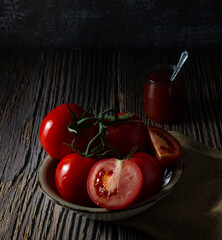 Delicious red ripe tomatoes on a wooden board and a jar of their traditional sauce. Dark food