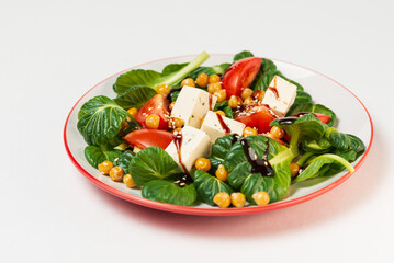 Fresh pak choi salad with tomatoes,chickpeas and feta cheese, poured with sauce and sesame seeds in a plate  isolated  on white