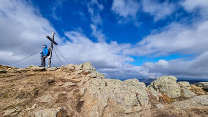 Man with hiking backpack standing at summit cross of mountain peak Ladinger Spitz, Saualpe,...