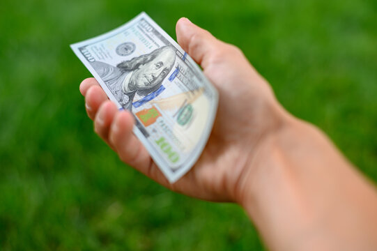 First person top view photo of hands holding fan of Dollar banknotes on park background
