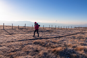 Silhouette of woman hiking on alpine frozen meadow along a fence after sunrise from Ladinger Spitz...