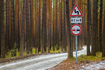 Road sign overtaking is prohibited at the turn of snow-covered highway. Two cars pass turn on the road among the trees.