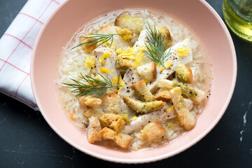 Soup with chicken breast, white rice, croutons and lemon zest served in a roseate bowl, middle close-up, selective focus