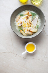 Bowl of chicken soup with croutons and rice, high angle view on a beige stone background, vertical shot with space