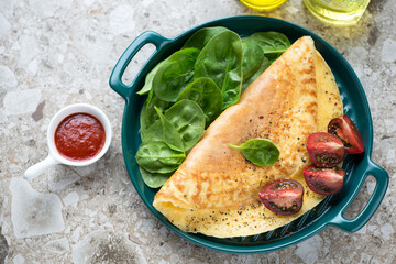 Omelet with fresh spinach leaves and tomatoes on a green serving tray, high angle view on a brown granite background