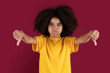 Disappointed african american kid showing thumb downs on colorful background