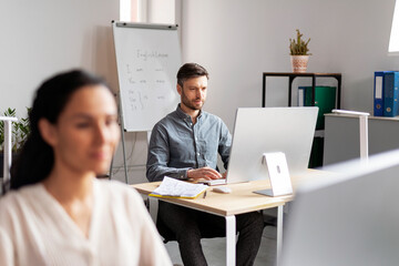 Serious busy handsome smiling millennial european woman and man managers working at computer