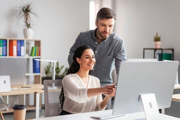Smiling millennial european female showing to man manager with hand in computer screen