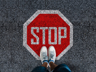 legs in sneakeers standing on asphalt road and stop sign